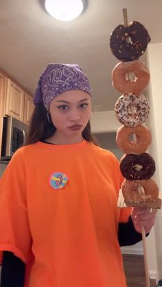 a girl in an orange shirt is holding two doughnuts on a wooden stick