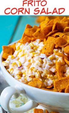 a white bowl filled with corn salad on top of a blue table next to chips