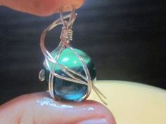 a person holding a wire wrapped pendant with a green bead on it's end