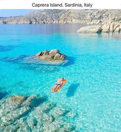 a person floating in the water with an orange floatie on their back, and some rocks