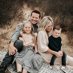 a man, woman and two children sitting on a blanket in the grass smiling at the camera