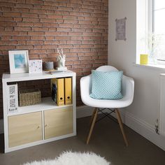 a white chair sitting in front of a brick wall next to a book shelf filled with books