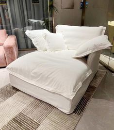 a white couch with pillows on it in front of a glass wall and two pink chairs