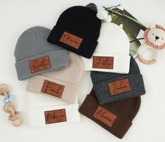 five beanies with leather labels on them are laid out next to a stuffed animal