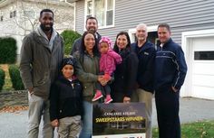 a group of people standing next to each other in front of a house with a sign