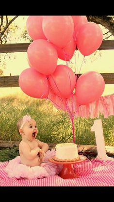 a baby is sitting in front of a cake with pink balloons on it and the number one