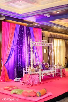 a stage set up with pink and purple drapes on the ceiling, white bed frame