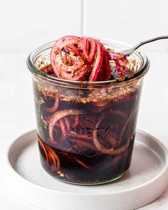 a jar filled with pickled onions on top of a white plate next to a spoon