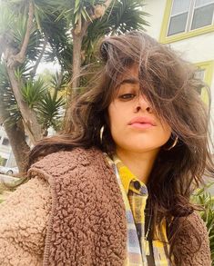 a woman standing in front of a tree with her hair blowing in the wind and wearing a jacket