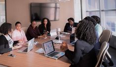 a group of people sitting around a table with laptops and papers in front of them