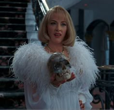 a woman in a white dress holding a skull and wearing an angel wings jacket with her hand