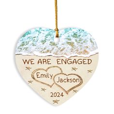 an ornament shaped like a heart with two hearts in the sand and words we are engaged