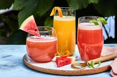 three glasses filled with different types of drinks on a tray next to watermelon slices