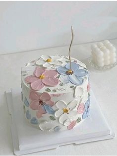 a white cake with flowers on it sitting on top of a table next to a candle