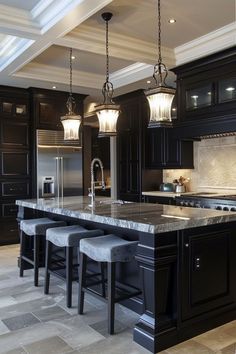 a large kitchen with black cabinets and marble counter tops on the center island is illuminated by pendant lights