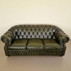 a green leather couch sitting on top of a tile floor next to a white wall