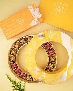 two plates with decorative designs on them next to a yellow gift box and some flowers