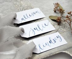 three place cards with names on them sitting on a table next to a flower and ribbon