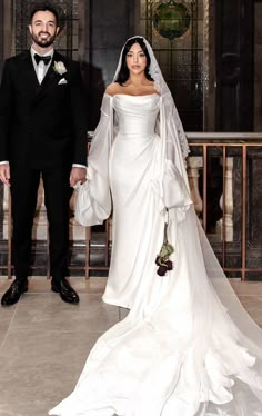 a man and woman in formal wear standing next to each other holding hands with the bride's veil draped over her shoulder