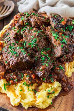 a wooden cutting board topped with meat and mashed potatoes covered in gravy