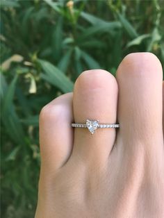 a woman's hand with a diamond ring on her finger and green plants in the background