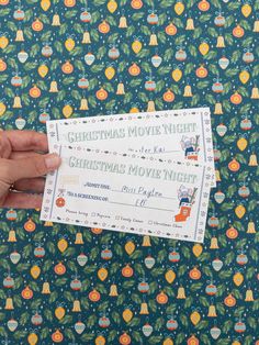 someone holding up a christmas movie night ticket in front of a wallpapered background