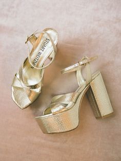 two pairs of gold high heeled shoes sitting on top of a pink sheet covered floor