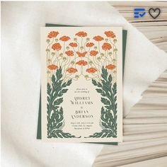 an orange and green floral wedding card on top of a white napkin with a heart in the background