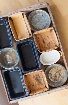 an open box filled with lots of dirty dishes on top of a wooden floor next to a table