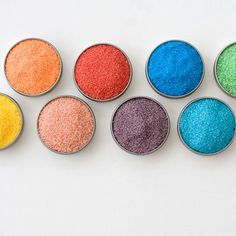 six small tins with different colored powder in them on a white surface, top view