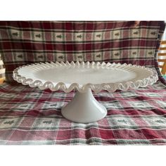 a white cake plate sitting on top of a plaid cloth covered tablecloth with a wooden chair in the background