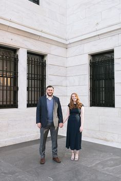 a man and woman standing next to each other in front of two large white buildings