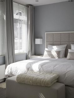 a white bed sitting in a bedroom next to two windows with blinds on each side