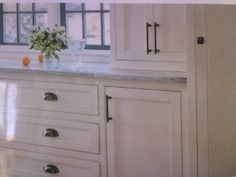 a kitchen with white cupboards and marble counter tops in front of a large window