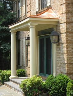 an old brick house with green doors and columns on the front porch, surrounded by shrubbery