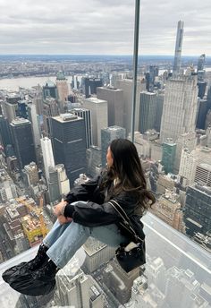 a woman sitting on top of a tall building looking out at the cityscape