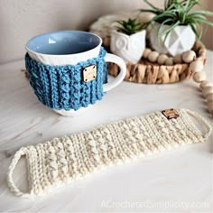 a knitted mug cozy sits next to a crocheted coffee cup holder on a table