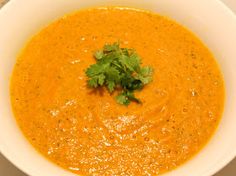 a white bowl filled with carrot soup and garnished with cilantro leaves