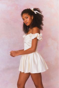 a woman in a short white dress posing for the camera with her hand on her hip