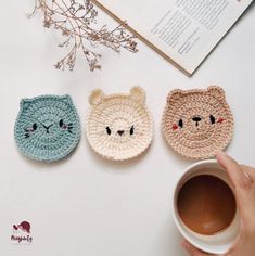 three crocheted animal coasters sitting on top of a table next to a cup of coffee