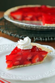 a slice of strawberry pie with whipped cream on top sitting on a plate next to another pie