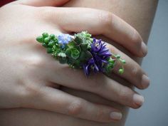 a woman's hand holding a ring with purple flowers on it and green leaves