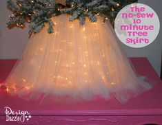 a pink table topped with a white christmas tree skirt and lots of lights on it