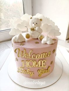 a pink cake with gold decorations and a teddy bear on top that says welcome home to the baby girl