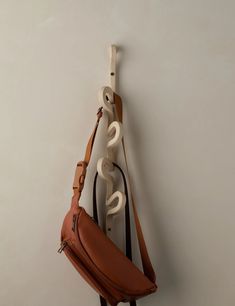 a brown leather bag hanging on the wall next to a white coat rack with hooks