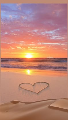 a heart drawn in the sand on a beach at sunset with waves coming in from the ocean