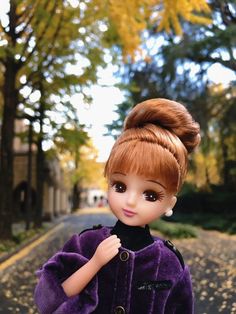 a doll is standing on the street with her hair in a bun and wearing a purple coat