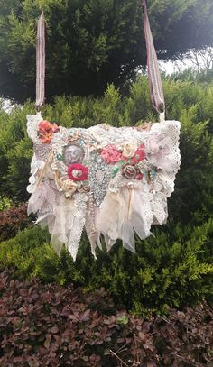 a handbag made out of lace and fabric with flowers on the front is hanging from a tree