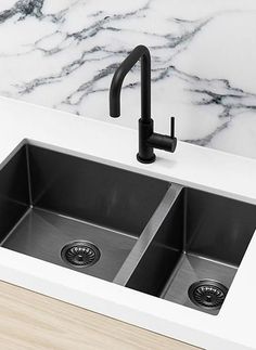 a kitchen sink with two black faucets and marble counter top in the background