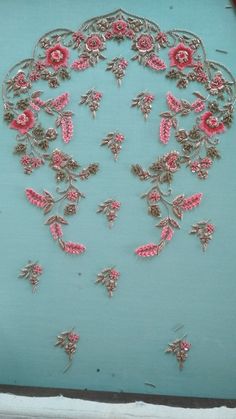 an embroidered piece with pink flowers and leaves in the center on a blue surface,